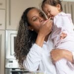 A loving mother feeds her child in a warm kitchen, capturing a moment of tenderness and care.