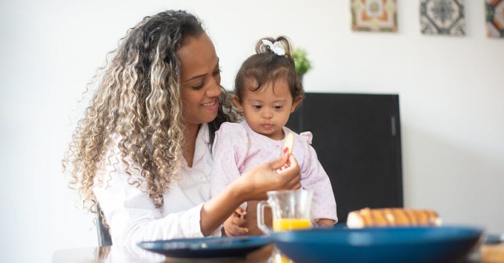 A loving mother feeds her young daughter breakfast at home, emphasizing care and togetherness.
