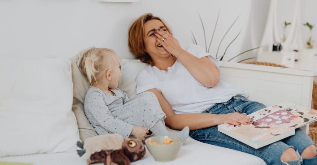 A joyful moment of a mother and child sharing laughs while reading together indoors.
