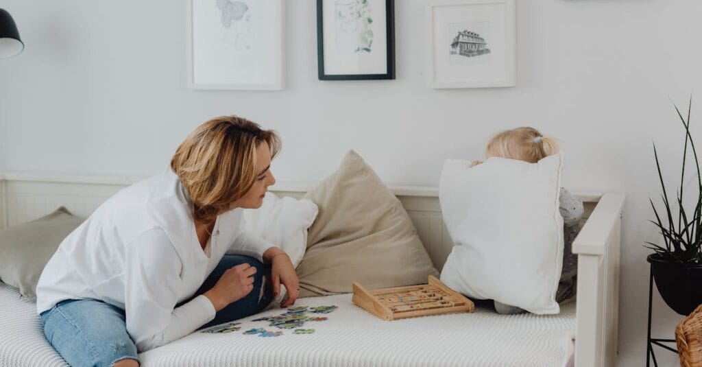 A mother interacting with her daughter hiding behind a pillow, enjoying quality time indoors.