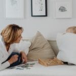 A mother interacting with her daughter hiding behind a pillow, enjoying quality time indoors.