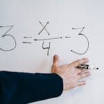 A hand writing a mathematical equation on a whiteboard with a marker.