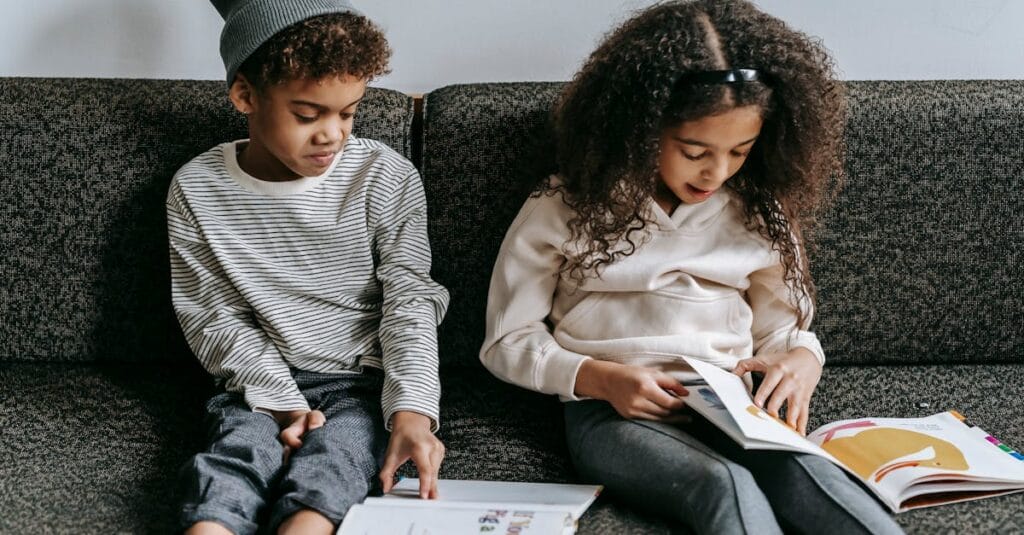 Grimacing stylish African American siblings reading books and sitting together on cozy couch in living room