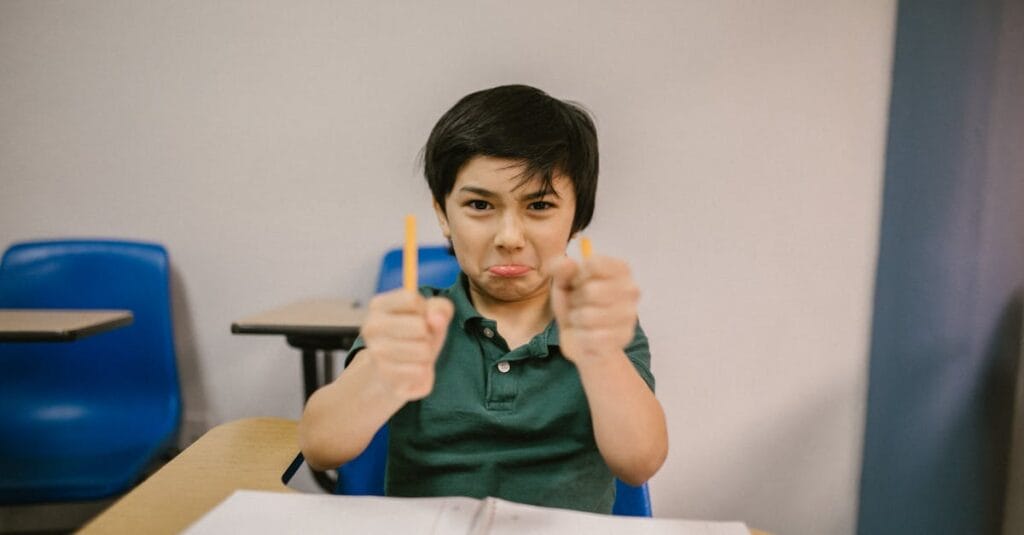 A young boy in a classroom showing frustration, holding broken pencils.