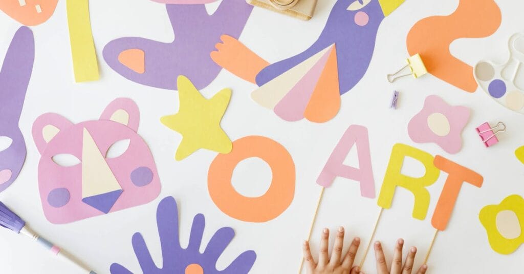 Creative art and craft layout with colorful paper cutouts and child’s hands, viewed from above.