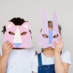 Two children wearing playful animal masks, showcasing creativity and imagination indoors.