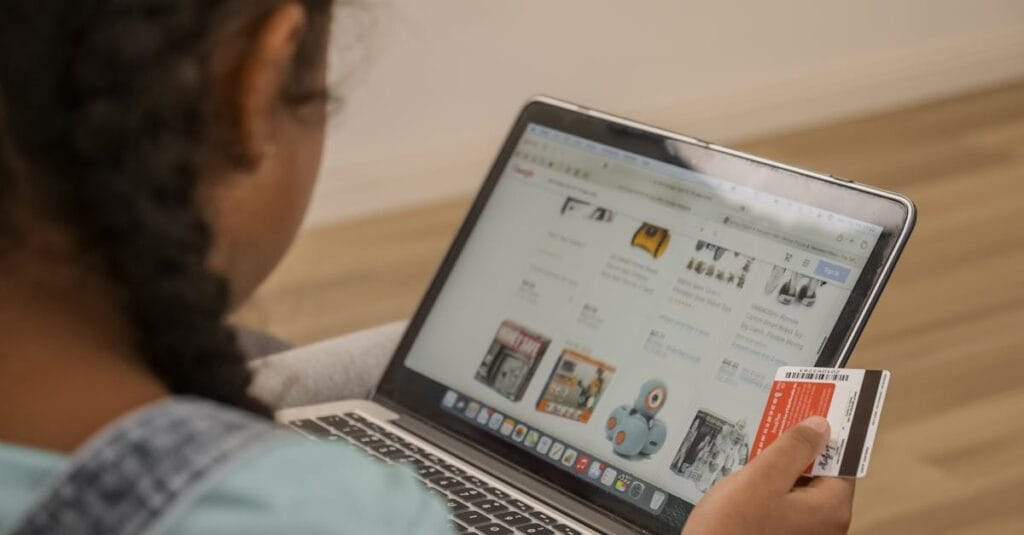Child using laptop for online shopping, holding a credit card.