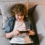 Young boy lying on sofa playing with a mobile device, smiling and relaxed indoors.