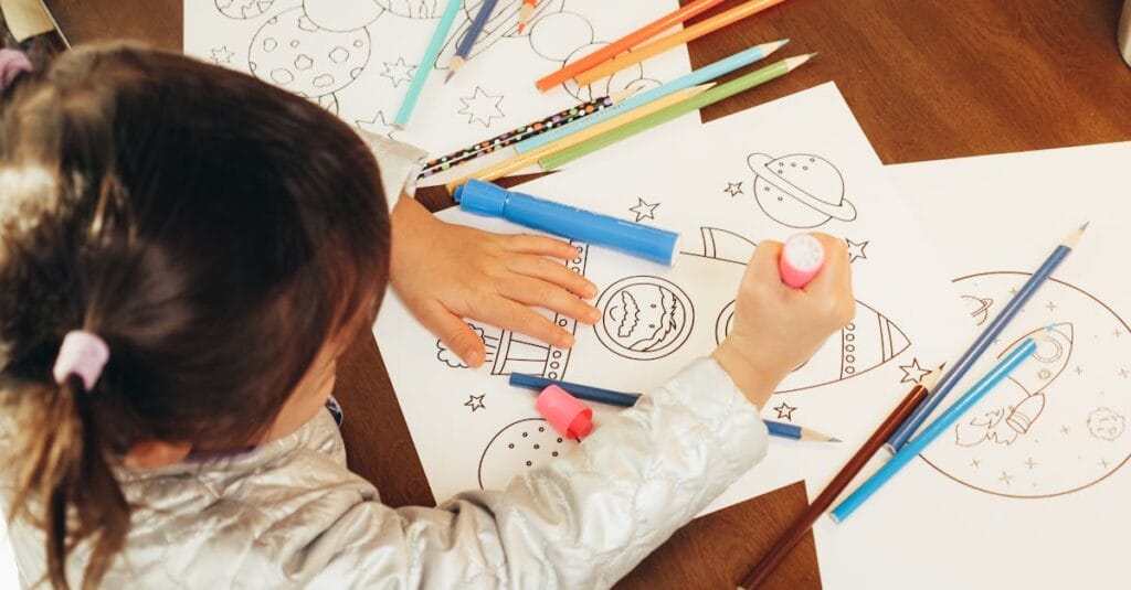 A child with pigtails coloring space-themed drawings with colorful pencils indoors.