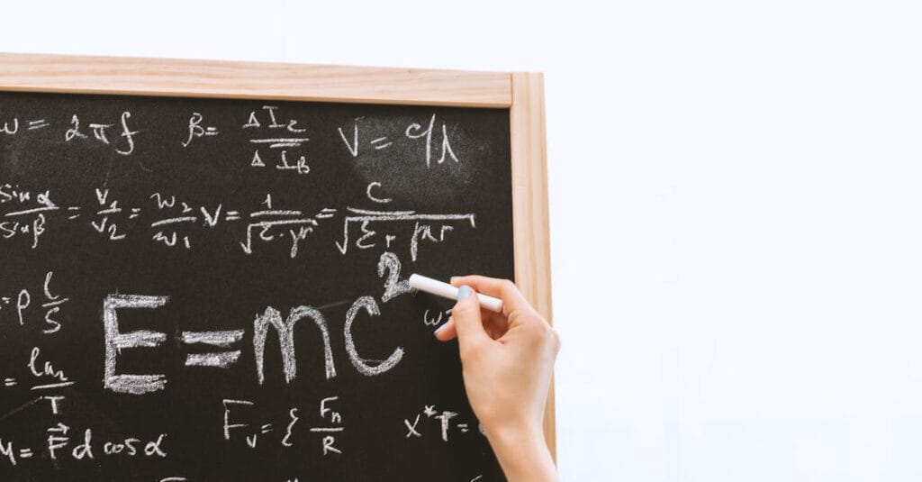 Close-up of hand writing physics equations on a chalkboard indoors.