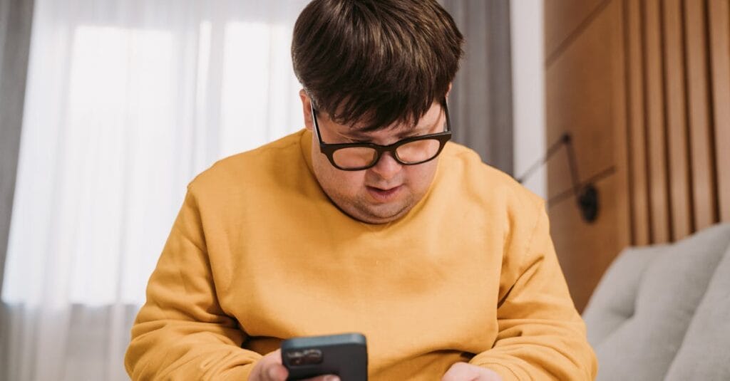 Man in yellow sweater using smartphone and credit card for online shopping indoors.