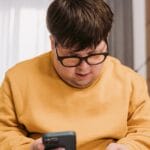 Man in yellow sweater using smartphone and credit card for online shopping indoors.