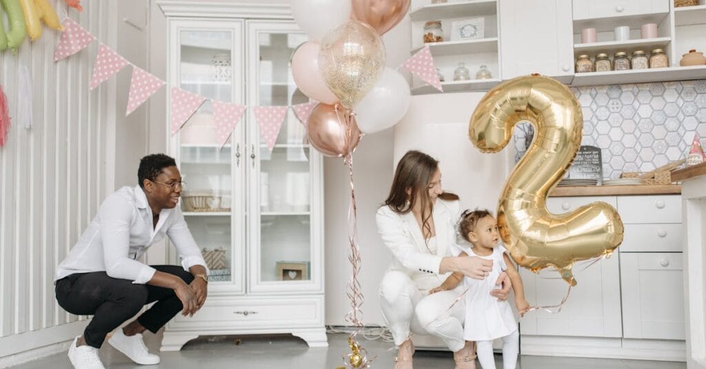 Family celebrating a child's second birthday in a decorated kitchen with balloons.