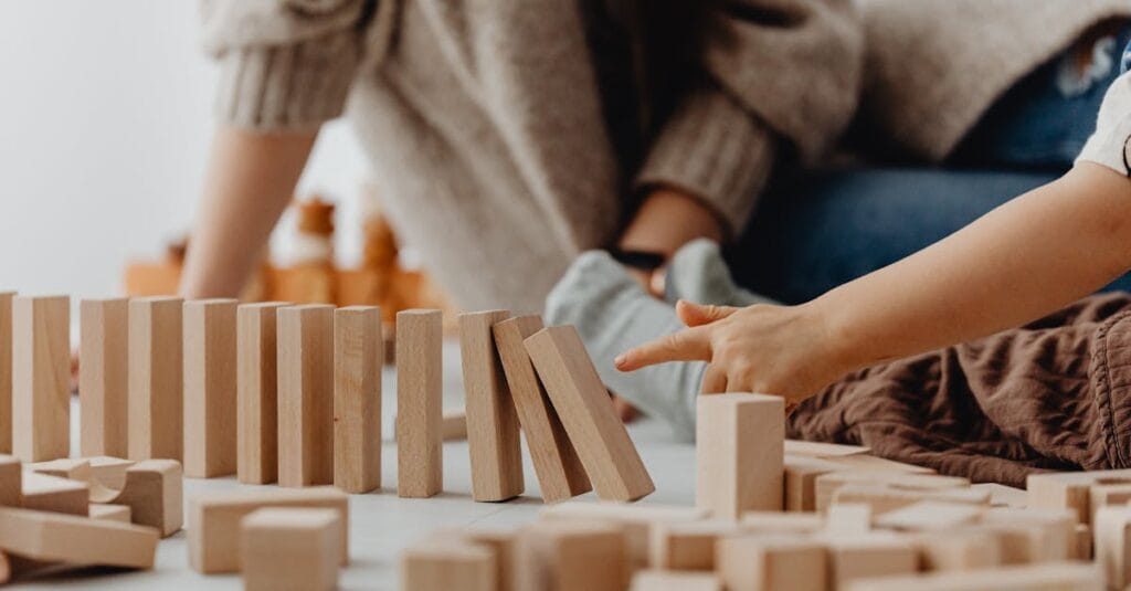Close-up of child's hand tipping over wooden blocks on a table indoors.