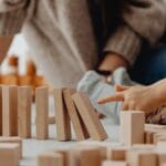 Close-up of child's hand tipping over wooden blocks on a table indoors.