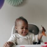 Cute baby in a high chair celebrating first birthday with balloons and decorations.