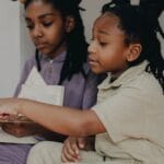 Two young sisters engaged in reading sheet music indoors, promoting education and togetherness.