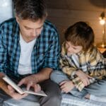 A father reads to his son on a bed, creating a warm family moment.