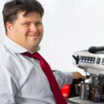 Man with Down syndrome smiling while making coffee at a cafe, symbolizing inclusivity.