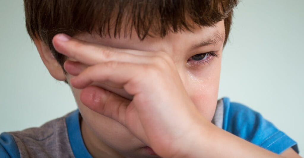 Close-up portrait of a young boy wiping away tears, expressing emotion.