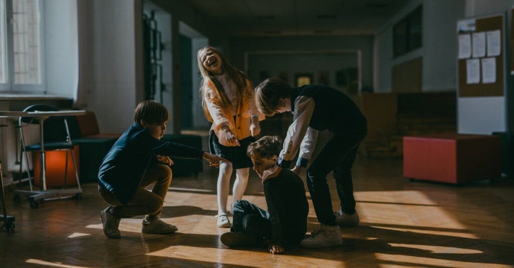 Group of children in a school setting pointing at a seated boy, highlighting school bullying dynamics.