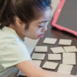 A young girl intently plays a memory card game indoors, showcasing focus and concentration.