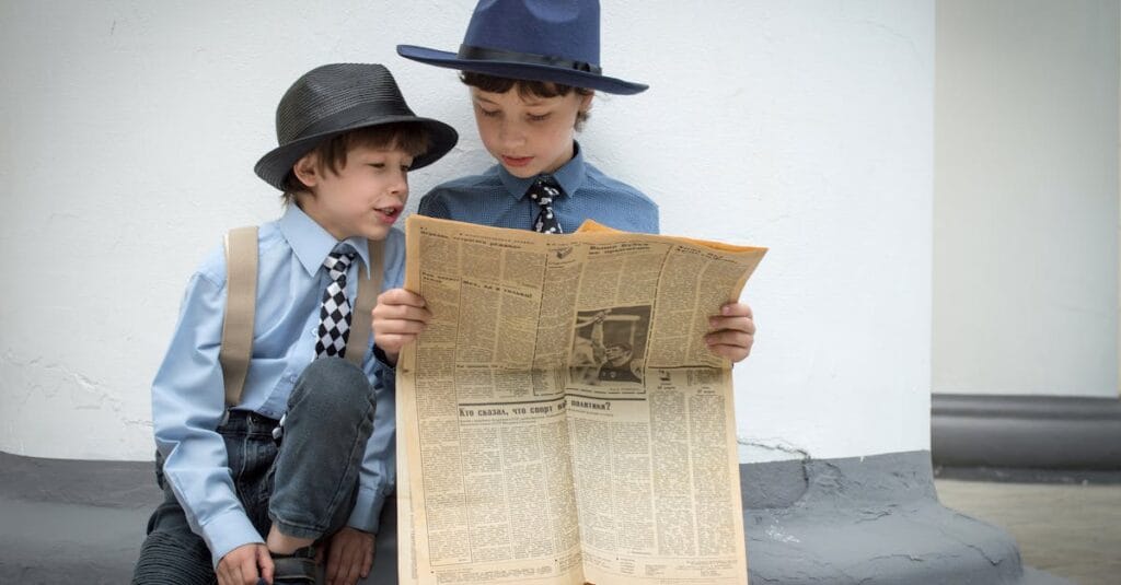 Two young boys in vintage attire reading a newspaper outdoors, sharing a thoughtful moment.