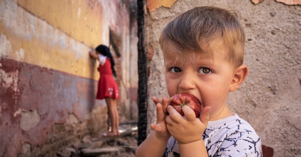 Young boy eating apple while playing hide and seek outdoors.