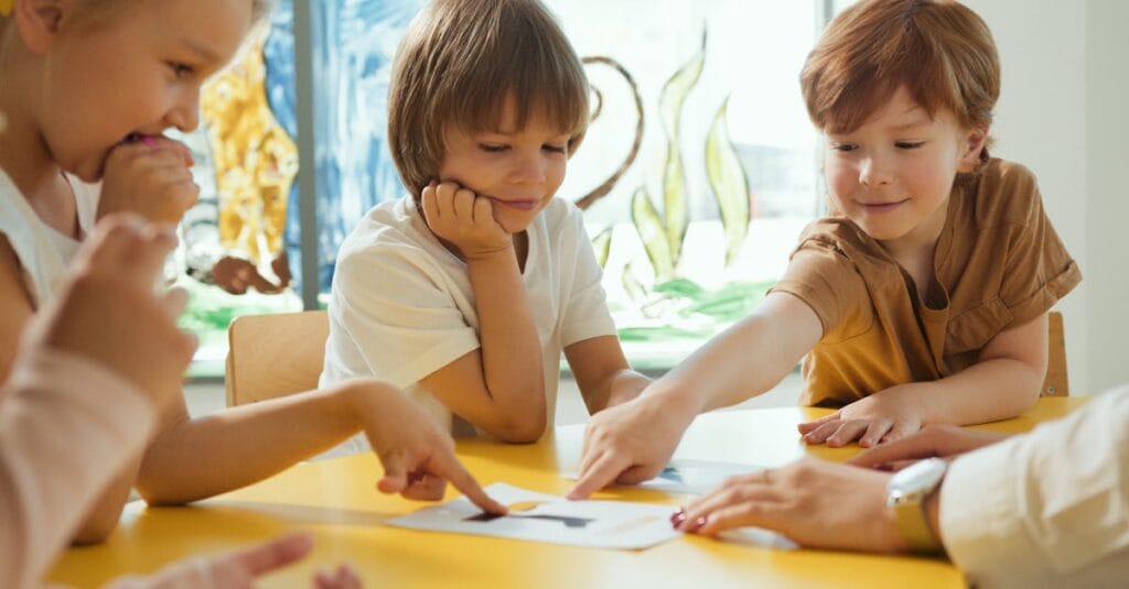 Young children engaging in fun learning activities at a yellow table in a classroom setting.