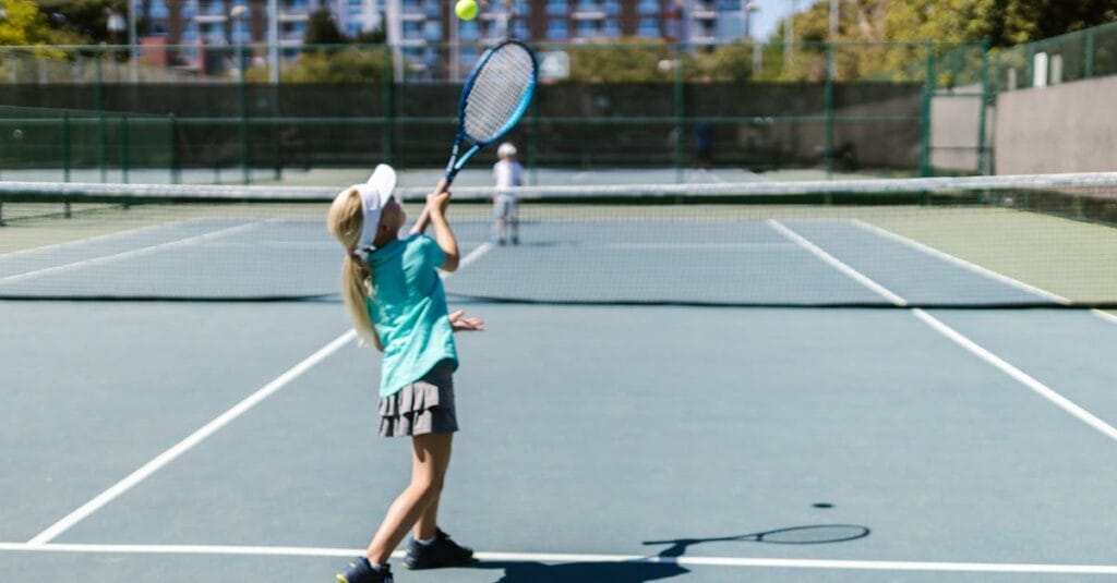 A girl in sportswear hitting a tennis ball on a sunny outdoor court.
