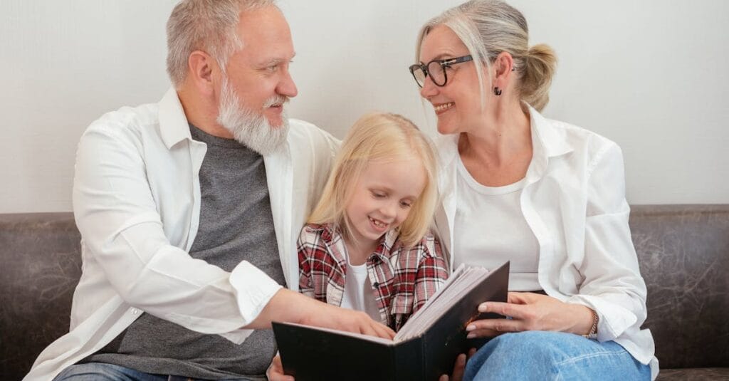 Happy grandparents reading a photo album with their granddaughter, creating cherished family memories.