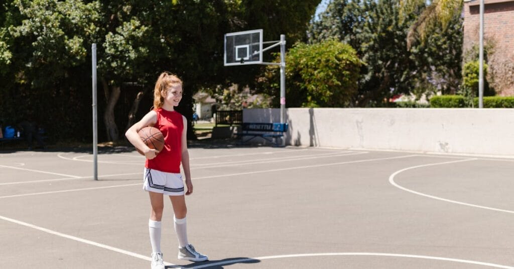 A young girl holding a basketball on an outdoor court, enjoying a sunny day.