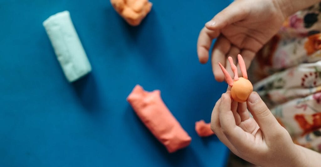Young hands shaping colorful clay into fun figures on a vibrant blue background.