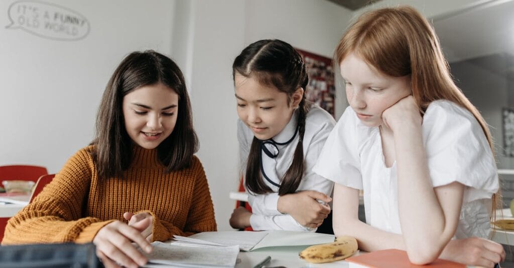 Three diverse schoolgirls working together over books in a classroom setting, fostering education and collaboration.