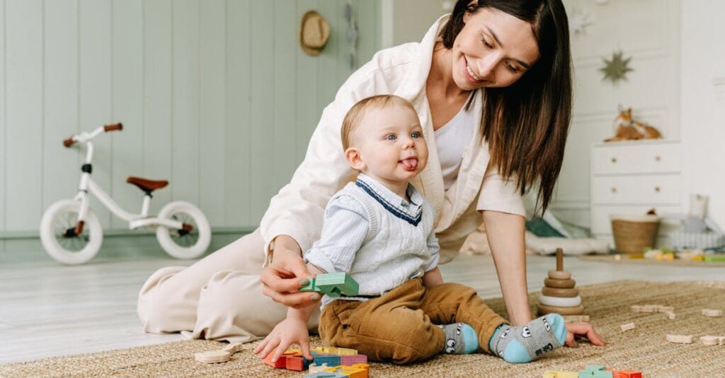 A joyful scene of a mother playing with her baby boy on the floor with colorful wooden blocks.