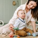 A joyful scene of a mother playing with her baby boy on the floor with colorful wooden blocks.