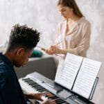 Young boy playing piano with female teacher guiding in a cozy home setting.