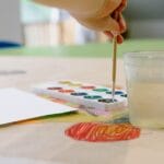 A child painting with watercolors in a bright, creative art classroom.