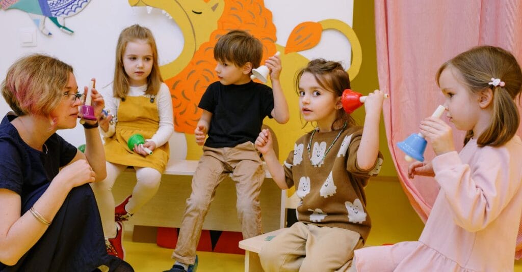 Young children playing musical bells in a colorful classroom setting with a teacher.