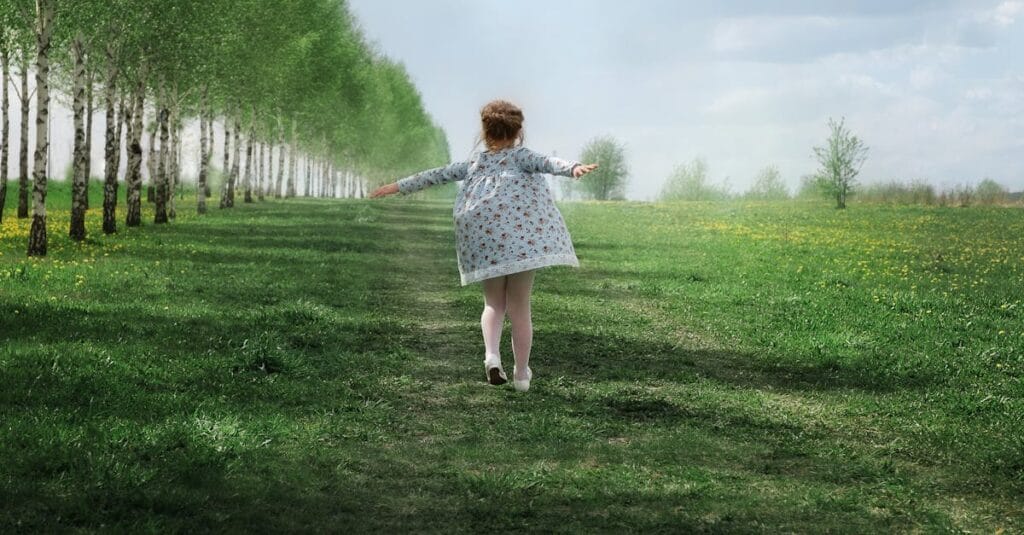 A child joyfully running down a tree-lined path in a lush green meadow on a sunny day.