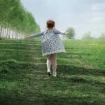 A child joyfully running down a tree-lined path in a lush green meadow on a sunny day.