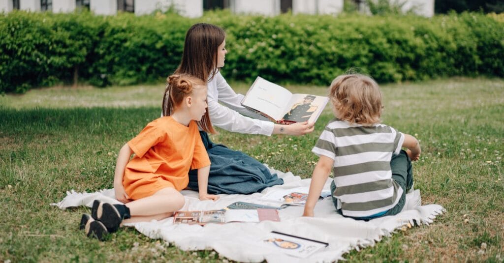 A woman teaching two children outdoors on a blanket, fostering education in nature.