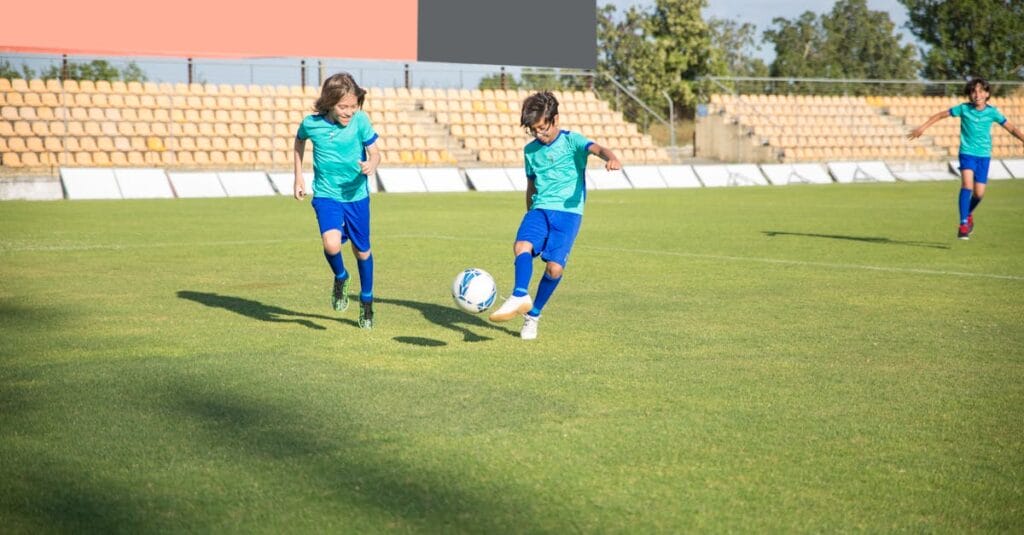 Children playing football on a sunny day in a Portuguese stadium.