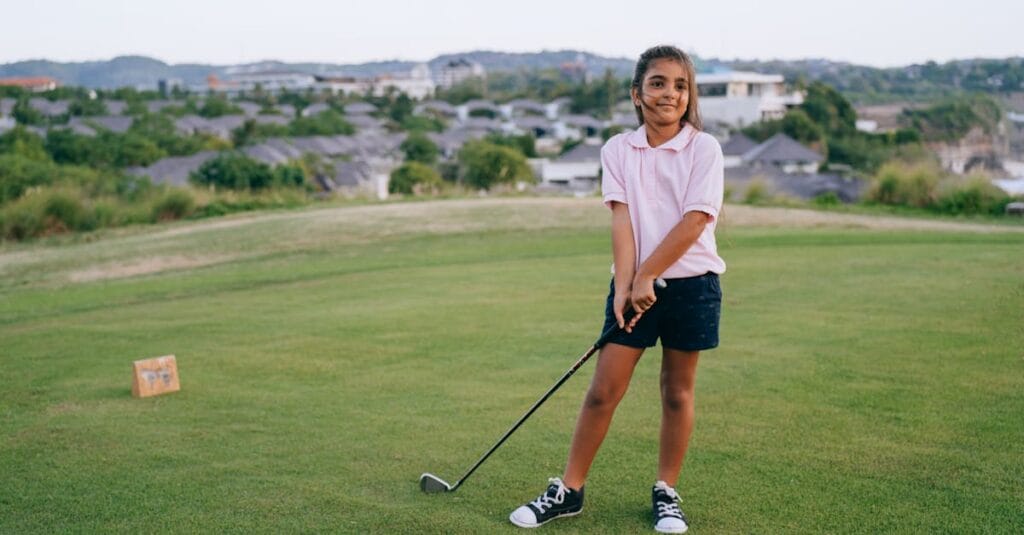 A smiling girl holding a golf club on an outdoor golf course, enjoying a sunny day.