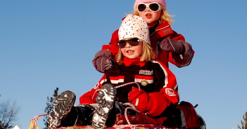 Two children enjoying a fun sled ride down a snowy hill on a sunny winter day.