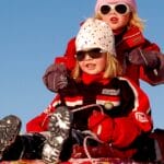 Two children enjoying a fun sled ride down a snowy hill on a sunny winter day.