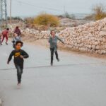 Group of kids running and playing on a rural street under a cloudy sky.
