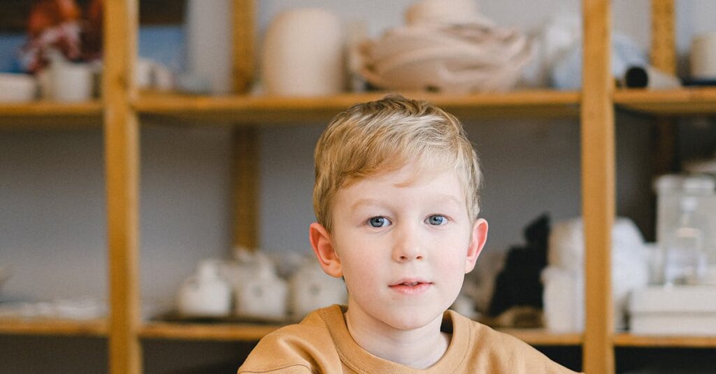 Young boy with blond hair drawing on a paper at a table indoors, wearing a brown sweater.