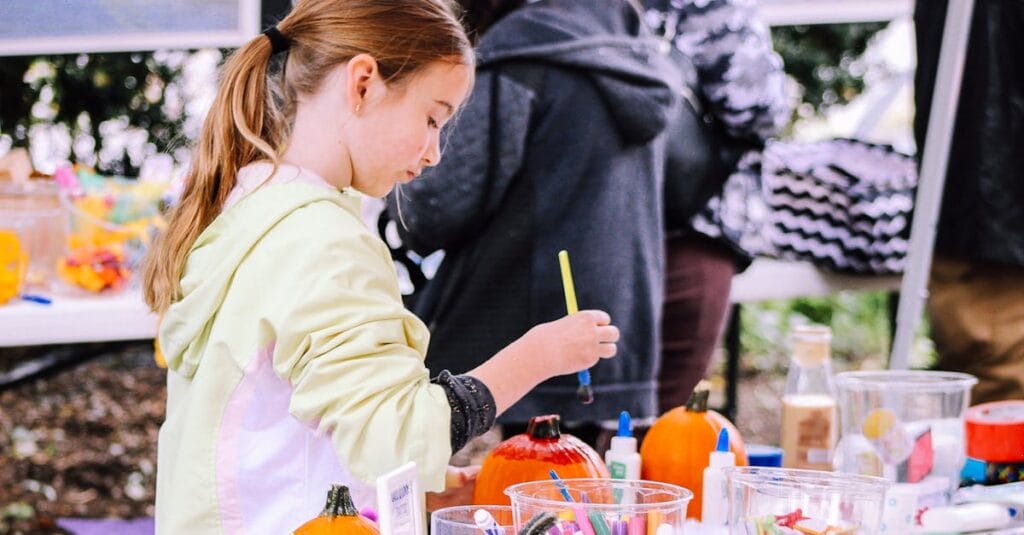 A child enjoys painting pumpkins at an outdoor crafting event, surrounded by art supplies.