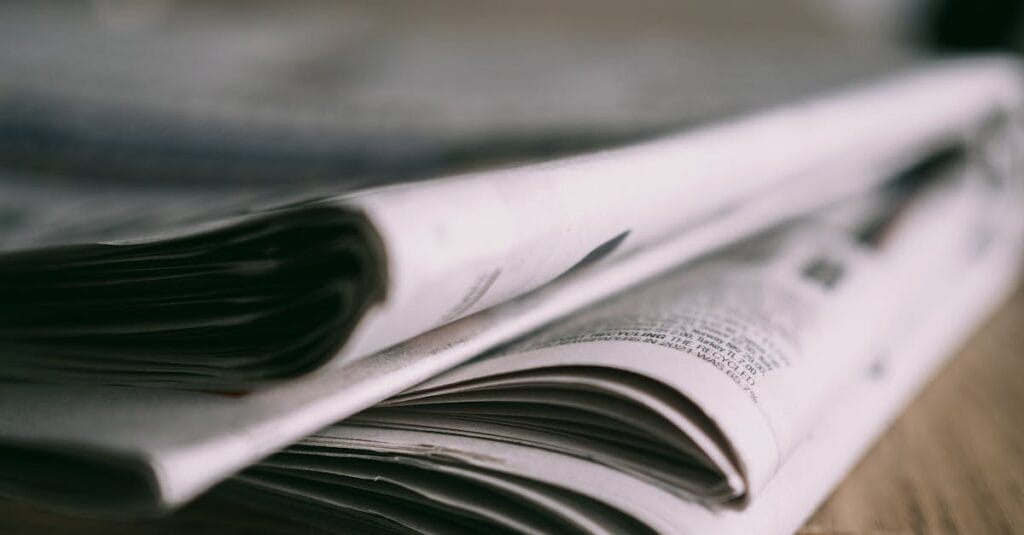 Stack of folded newspapers on a wooden table with a focus on printed pages.